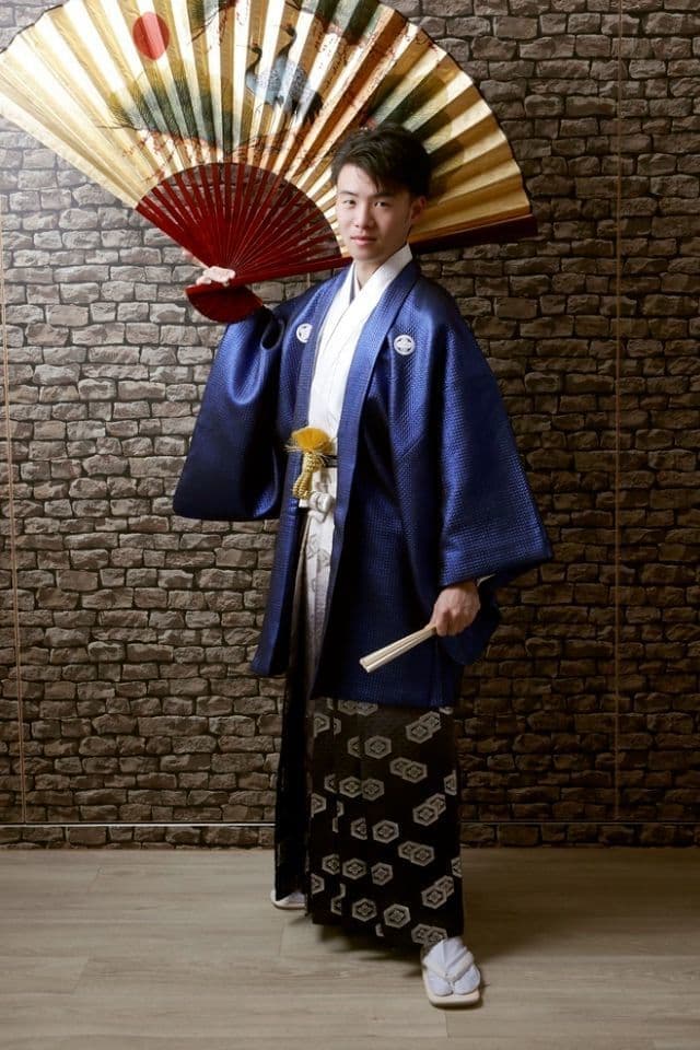 成人式に紋服和装を着た男性が大きな扇子を持ち立っている姿